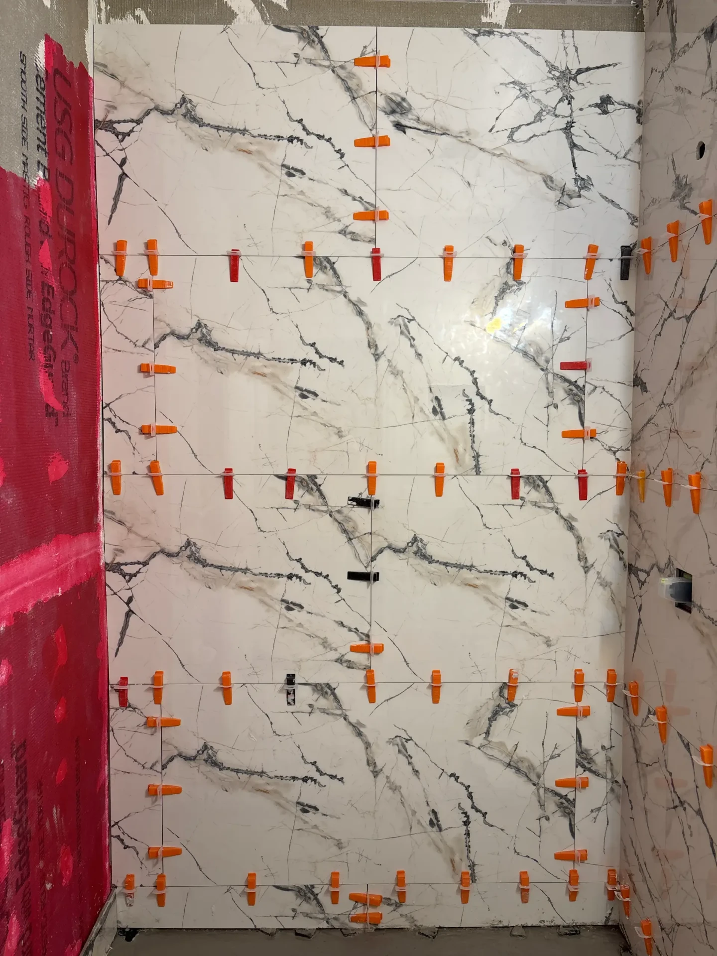 Large-format porcelain tile set with leveling clips on the shower wall